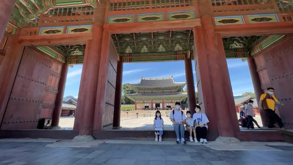 A family of four sitting and taking photos in front of Injeongmun Gate at Changdeokgung Palace, Seoul, South Korea